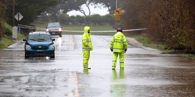 San Luis Obispo County workers forecast flooding on a road in Cambria, California, on Thursday, January 28, 2021. After losing land on Tuesday in northern California, a storm aimed at the central coast, where the two-day-long precipitation approached a total of 14 inches (35.5 centimeters) in San Luis Obispo County, according to the National Weather Service. (Laura Dickinson / The Tribune (by San Luis Obispo) via AP)