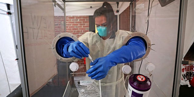 BOSTON, MA - JANUARY 7: An LPN puts away a patient testing kit from behind a plexiglass compartment at a walk-up COVID-19 testing site at a tent on the North Bennet Street alleyway in Boston's North End on Jan. 7, 2021. 