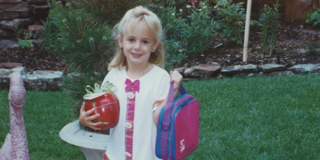 JonBenet Ramsey holds a backpack and plastic apple in an undated family photo.