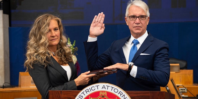 In this photo provided by the County of Los Angeles, incoming Los Angeles County District Attorney George Gascon is sworn in as his wife Fabiola Kramsky holds a copy of the Constitution during a mostly-virtual ceremony in downtown Los Angeles Monday, Dec. 7, 2020.  (Bryan Chan/County of Los Angeles via AP)