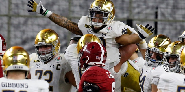Notre Dame running back Kyren Williams, top, is lifted by offensive lineman Landon Dickerson (69) after Williams' touchdown run as Alabama linebacker Christian Harris (8) looks on in the first half of the Rose Bowl NCAA college football game in Arlington, Texas, Jan. 1. (AP Photo/Roger Steinman)