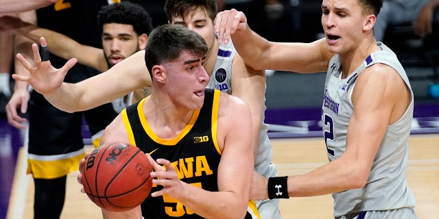 Iowa center Luka Garza (55) looks to pass against Northwestern forward Pete Nance, right, and center Ryan Young during the first half of an NCAA college basketball game in Evanston, Ill., Sunday, Jan. 17, 2021. (AP Photo/Nam Y. Huh)