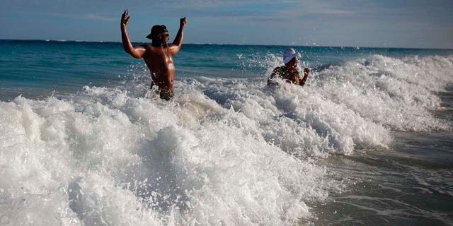 U.S. tourist Latron Evans and his partner Nika, frolicking ocean waters at the beach in Tulum, Quintana Roo state, Mexico, Monday, Jan. 4, 2021. Evans, a Mississippi firefighter, said he was impressed by the health measures due to the new coronavirus pandemic. (AP Photo/Emilio Espejel)