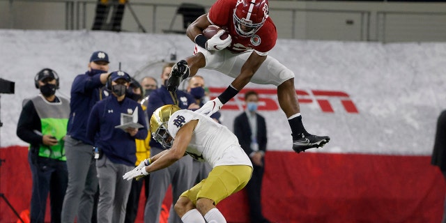 Alabama running back Najee Harris (22) hurdles Notre Dame cornerback Nick McCloud (4) as he carries the ball for a long gain in the first half of the Rose Bowl NCAA college football game in Arlington, Texas, Jan. 1, 2021. (AP Photo/Michael Ainsworth)