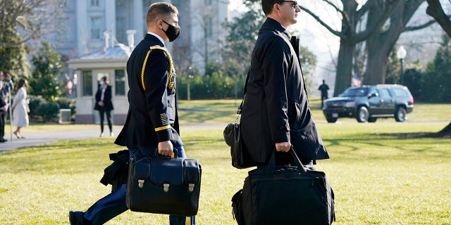 A U.S. military aide, left, carries the "President's emergency satchel," also know as "the football," with the nuclear launch codes, as President Donald Trump walks to board Marine One on the South Lawn of the White House, Tuesday, Jan. 12, 2021, in Washington. (AP Photo/Gerald Herbert )