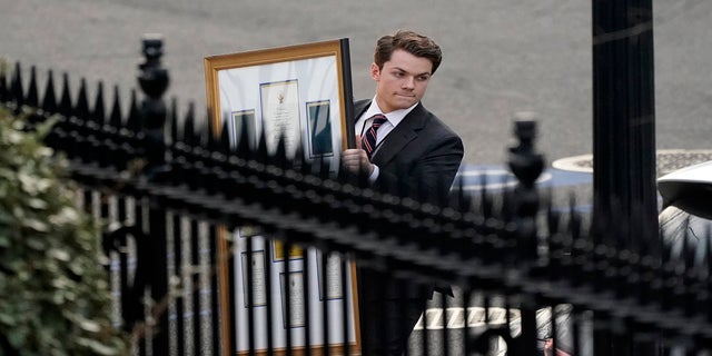 A man carries framed items to a car as he leave the Eisenhower Executive Office building on Thursday. (AP)