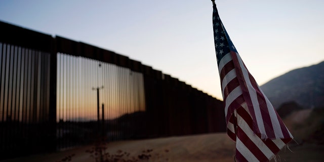 FILE - In this Sept. 24, 2020, file photo a flag sits just north of a new section of the border structure, behind,, near Tecate, Calif. The Trump administration sought to halt migrants from crossing the southwest border through measures that included forcing people seeking asylum to do to so in Mexico or Central America and building about 450 miles of wall. . (AP Photo/Gregory Bull)