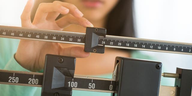 Woman adjusts the balance to find out her weight on a scale.