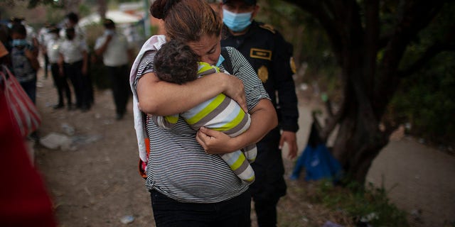 A woman carries her son as Honduran migrants confront Guatemalan soldiers and police manning a roadblock that prevents them from advancing toward the US, on the highway in Vado Hondo, Guatemala, Monday, Jan. 18, 2021. (AP Photo/Sandra Sebastian)