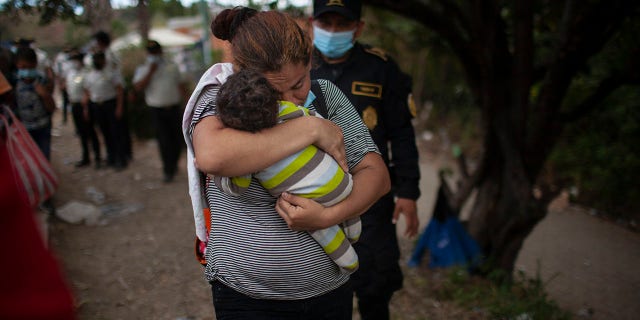 A woman carries her son as Honduran migrants confront Guatemalan soldiers and police manning a roadblock that prevents them from advancing toward the US, on the highway in Vado Hondo, Guatemala, Monday, Jan. 18, 2021. (AP Photo/Sandra Sebastian)