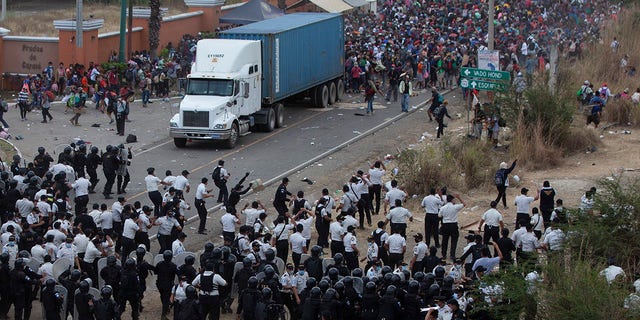 Honduran migrants, top, stand behind a cargo truck as they confront Guatemalan soldiers and police blocking them from advancing toward the US, on the highway in Vado Hondo, Guatemala, Monday, Jan. 18, 2021. (AP Photo/Sandra Sebastian)