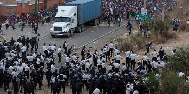 Honduran migrants, top, stand behind a cargo truck as they confront Guatemalan soldiers and police blocking them from advancing toward the US, on the highway in Vado Hondo, Guatemala, Monday, Jan. 18, 2021. (AP Photo/Sandra Sebastian)