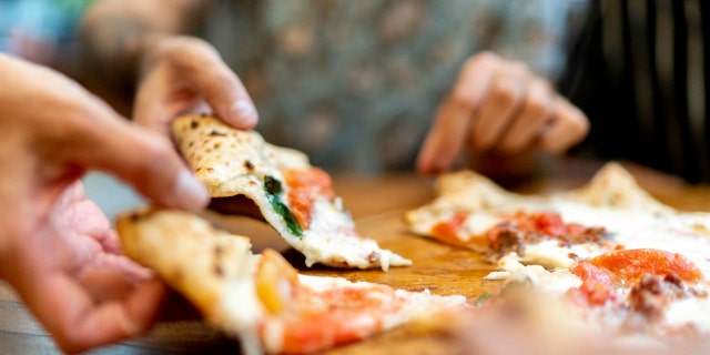 Friends getting slices of pizza, using hands