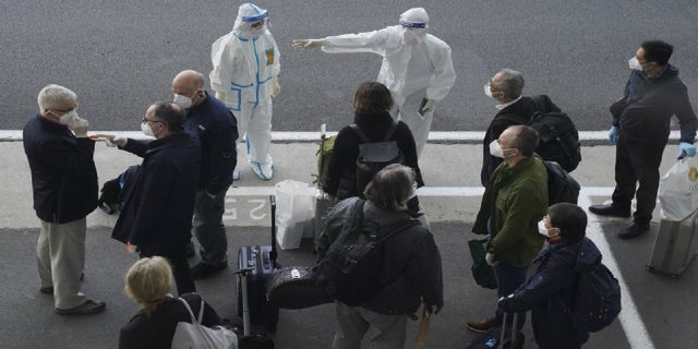 A worker in protective coverings directs members of the World Health Organization (WHO) team on their arrival at the airport in Wuhan in central China's Hubei province on Thursday, Jan. 14, 2021. (AP Photo/Ng Han Guan) (AP Photo/Ng Han Guan)