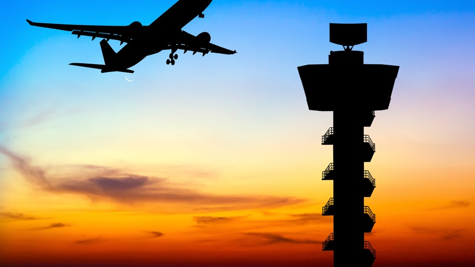 airplane flying by tower at sunset