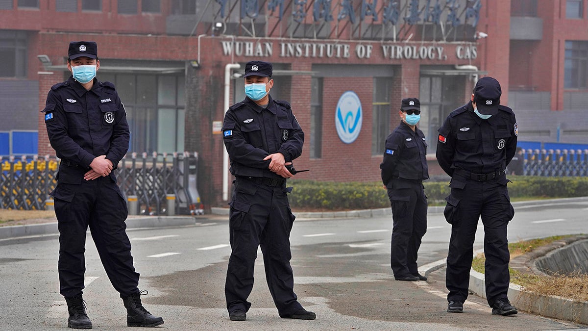 Guards in black uniforms stand in front of a building marked, "Wuhan Institute of Virology"