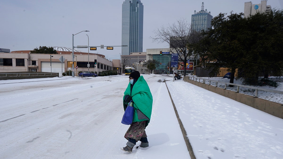 A woman wrapped in a blanket crosses the street near downtown Dallas, Tuesday, Feb. 16, 2021. Temperatures dropped into the single digits as snow shut down air travel and grocery stores. (AP Photo/LM Otero)