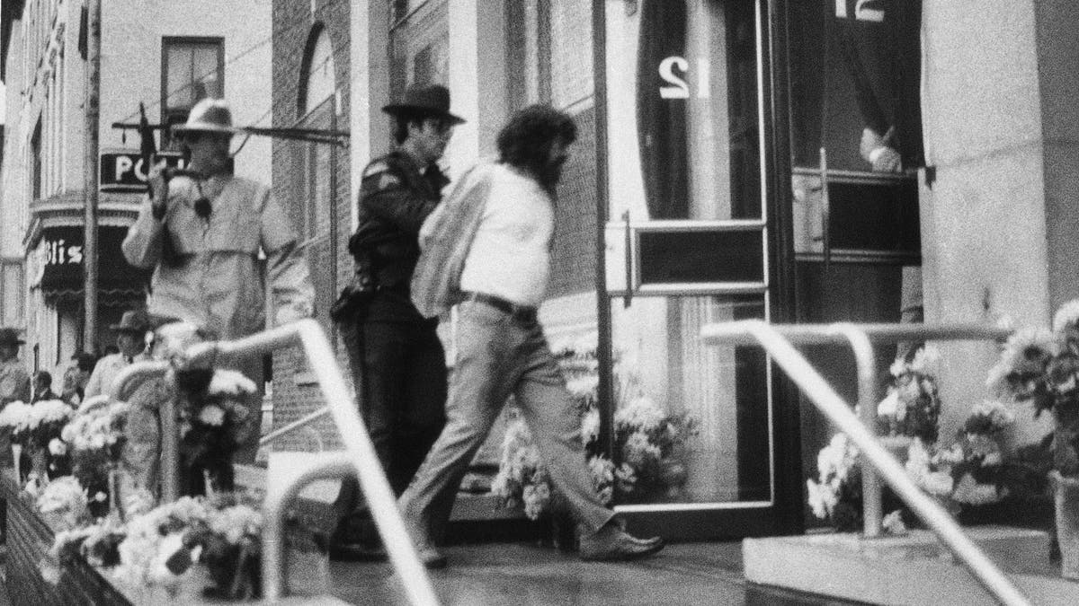 In this Oct. 24, 1981, file photo, David J. Gilbert, right, is escorted by police into the Village Hall in Nyack, N.Y., for a hearing on felony murder charges stemming from the Oct. 20, 1981, Brink's armored car robbery at a mall in Nanuet, N.Y., and a subsequent shootout with Nyack police that left three people dead. Now 76 years old, Gilbert is still imprisoned in New York state after nearly four decades. Gilbert's son, San Francisco chief District Attorney Chesa Boudin, and other allies are lobbying for clemency for Gilbert as coronavirus cases rise among prison inmates. (AP Photo/David Handschuh, File)