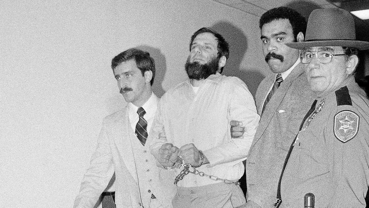 In this Nov. 23, 1981, file photo, Rockland County and others lead a handcuffed David Gilbert from Rockland County Court in New City, N.Y., after a hearing in Gilbert's felony murder case. Gilbert was convicted of murder in the deaths of two Nyack police officers and a Brink's guard during an infamous botched robbery considered one of the last gasps of '60s radicalism. Gilbert's son Chesa Boudin, now the San Francisco chief district attorney, and others are seeking clemency from New York Gov. Andrew Cuomo for Gilbert, now 76 and still imprisoned for the Oct. 20, 1981, robbery. The case is more pressing due to the increased risk of COVID-19 among prisoners. (AP Photo/David Handschuh, File)