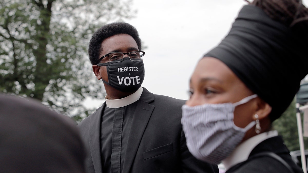 FILE - In this Monday, July 20, 2020 file photo, the Rev. Rahsaan Hall, of the St. Paul AME Church in Cambridge, Mass., wears a mask which reads, "Register &amp; Vote" outside the Statehouse in Boston. (AP Photo/Charles Krupa)