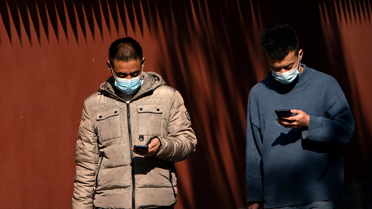 People wearing face masks to protect against the spread of the coronavirus use their smartphones as they walk through Ditan Park in Beijing, Tuesday, Feb. 9, 2021. China's internet watchdog is cracking down further on online speech, issuing a new requirement that bloggers and influencers have a government-approved credential before they can publish on certain topics. (AP Photo/Mark Schiefelbein)