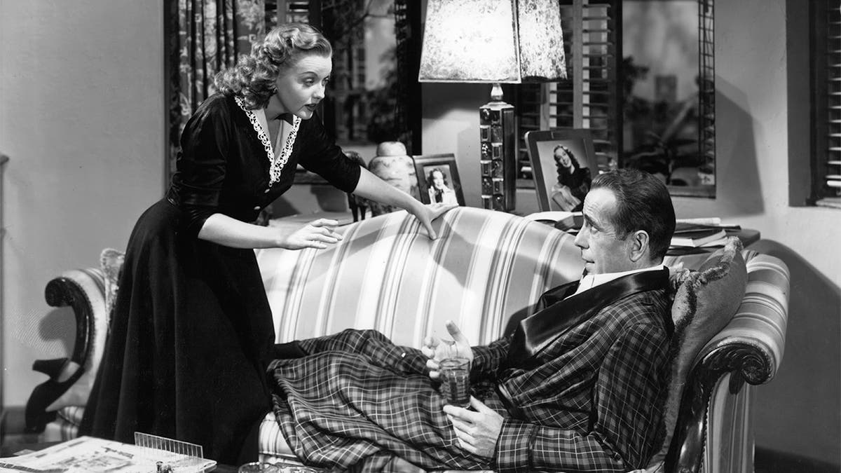 Martha Stewart talks to Humphrey Bogart who's lying on the couch in a scene from the film 'In a Lonely Place', 1950.
