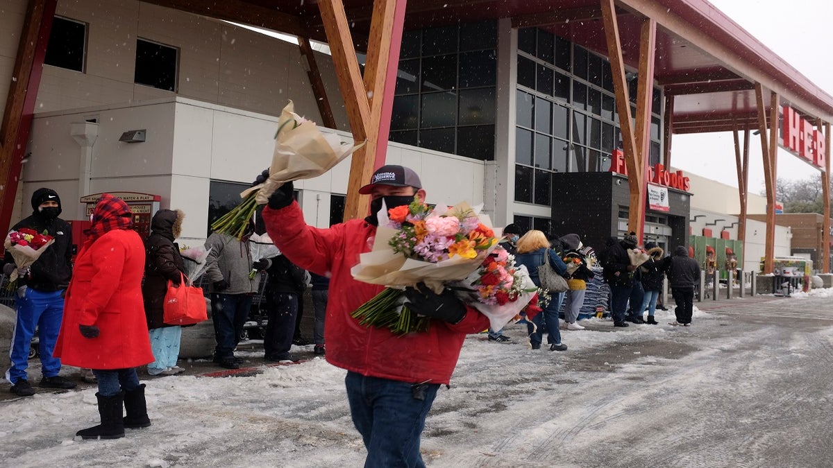 An HEB grocery store employee hands out flowers to customers waiting in line in the snow Thursday in Austin, Texas. (AP)