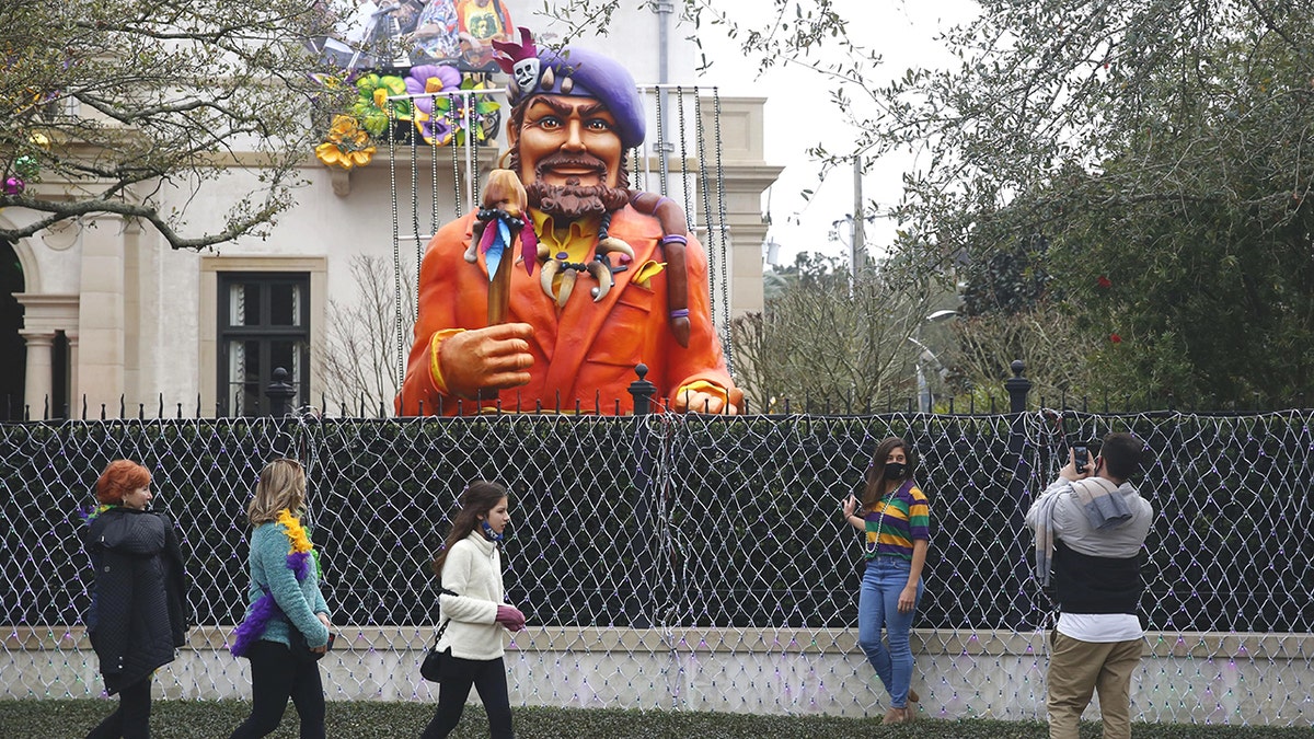 Passersby stop for photos in front of a house decorated for Mardi Gras. 