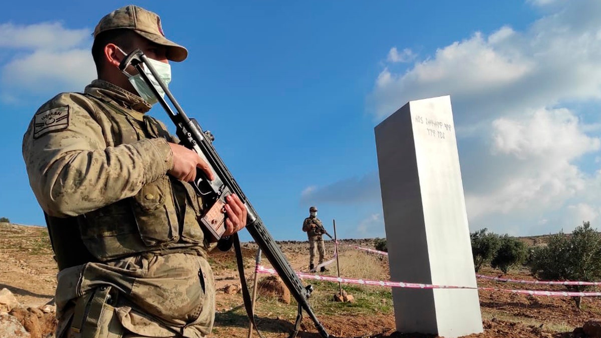 Turkish police officers guard a monolith, found on an open field near Sanliurfa, southeastern Turkey, Sunday, Feb. 7, 2021. The metal block was found by a farmer Friday in Sanliurfa province with old Turkic script that reads "Look at the sky, see the moon." The monolith, 3 meters high (about 10 feet), was discovered near UNESCO World Heritage site Gobeklitepe with its megalithic structures dating back to 10th millennium B.C. Turkish media reported Sunday that gendarmes were looking through CCTV footage and investigating vehicles that may have transported the monolith. Other mysterious monoliths have popped up and some have disappeared in numerous countries since 2020. (Bekir Seyhanli/IHA via AP)