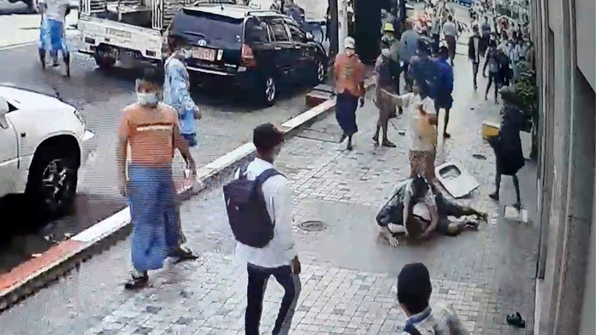 In this image taken from video obtained by Than Lwin Khet News, a woman helps an unidentified man lying on the sidewalk of Sule Pagoda Road after he was attacked by a group of men in Yangon, Burma, on Thursday. (Than Lwin Thet News via AP)