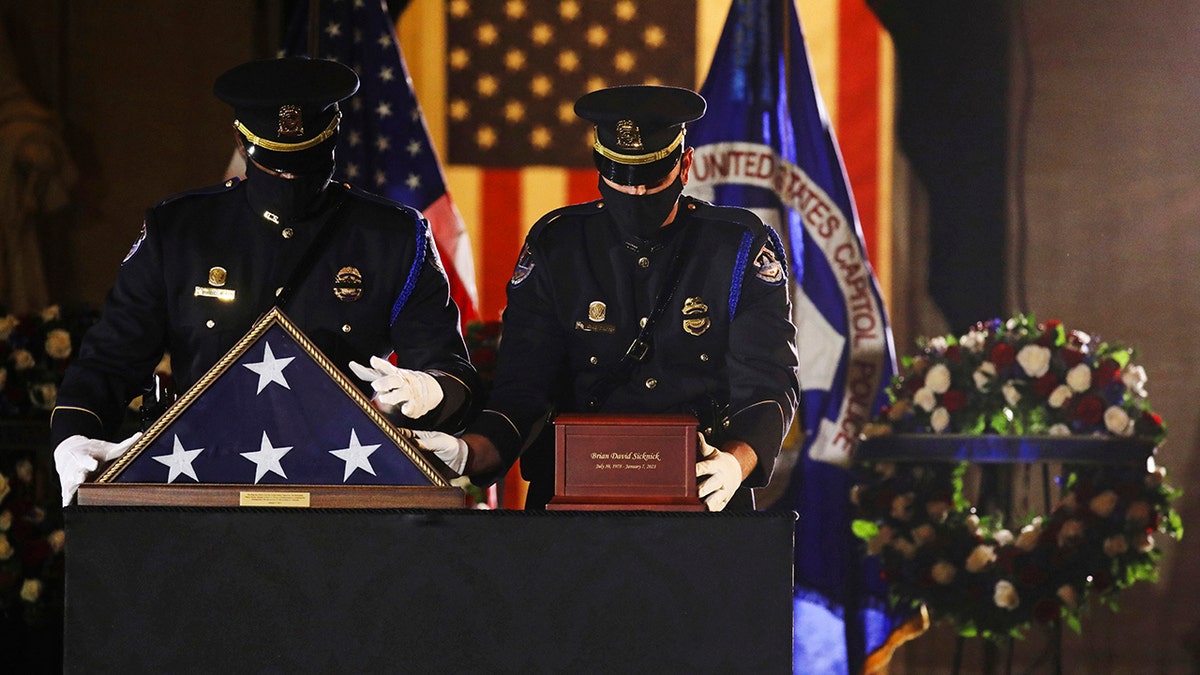 An honor guard places an urn with the cremated remains of U.S. Capitol Police officer Brian Sicknick and folded flag on a black-draped table at the center of the Capitol Rotunda Tuesday, Feb. 2, 2021, in Washington. (Leah Millis/Pool via AP)