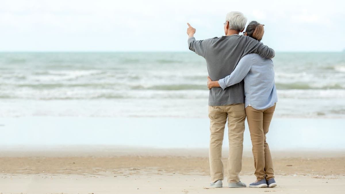 Asian Lifestyle senior couple hug and pointing on the beach happy in love romantic and relax time.  People tourism elderly family travel leisure and activity after retirement in vacations and summer, copy space and banner (iStock)