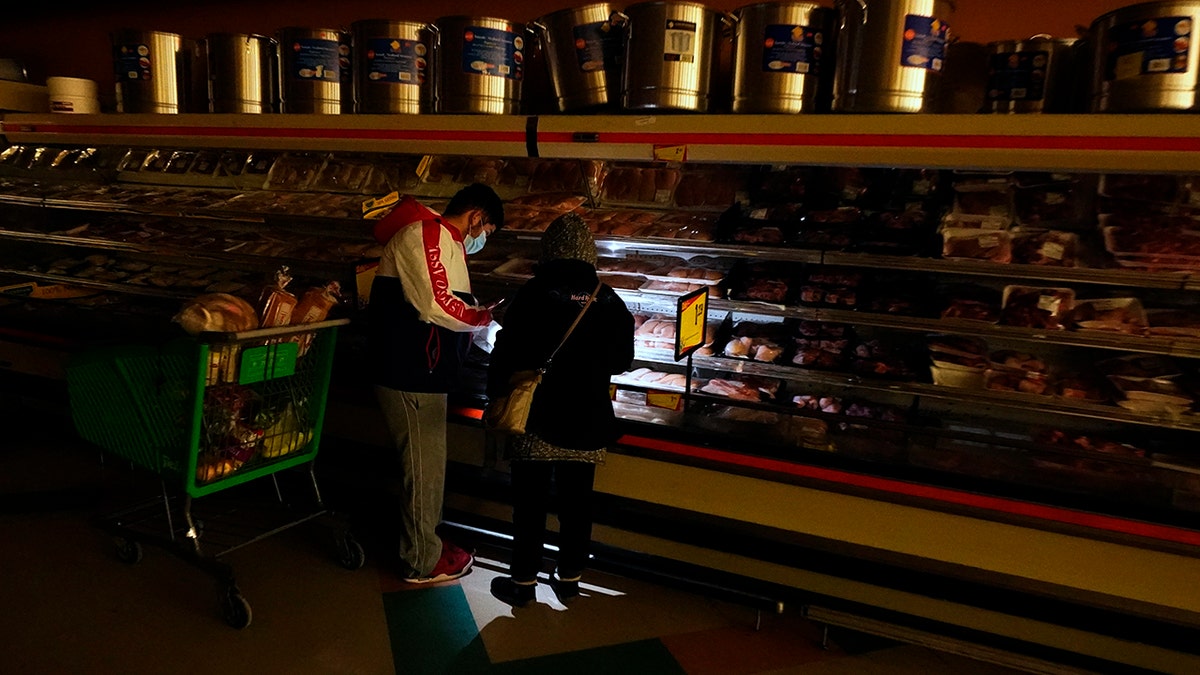 Customers use the light from a cellphone to look in the meat section of a grocery store Tuesday, Feb. 16, 2021, in Dallas. Even though the store lost power, it was open for cash-only sales.