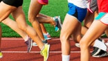 A girls cross country team running on a red track at the start of practice on a early summer evening.