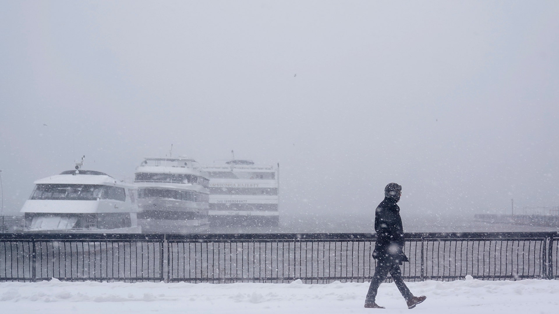 A man walks along a waterfront that usually has a view of the New York City skyline in Hoboken, N.J., Monday, Feb. 1, 2021. A sprawling, lumbering winter storm is walloping the Eastern U.S., shutting down coronavirus vaccination sites, closing schools and halting transit. (AP Photo/Seth Wenig)