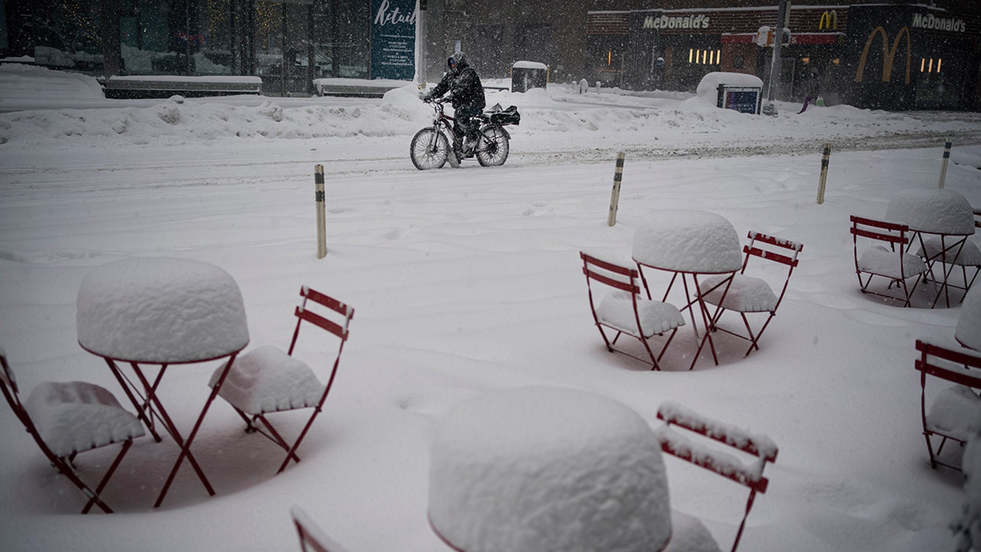 A man delivers food on his electric bicycle as he rides past snow-covered dining tables in Midtown during a snowstorm, Monday, Feb. 1, 2021, in New York.