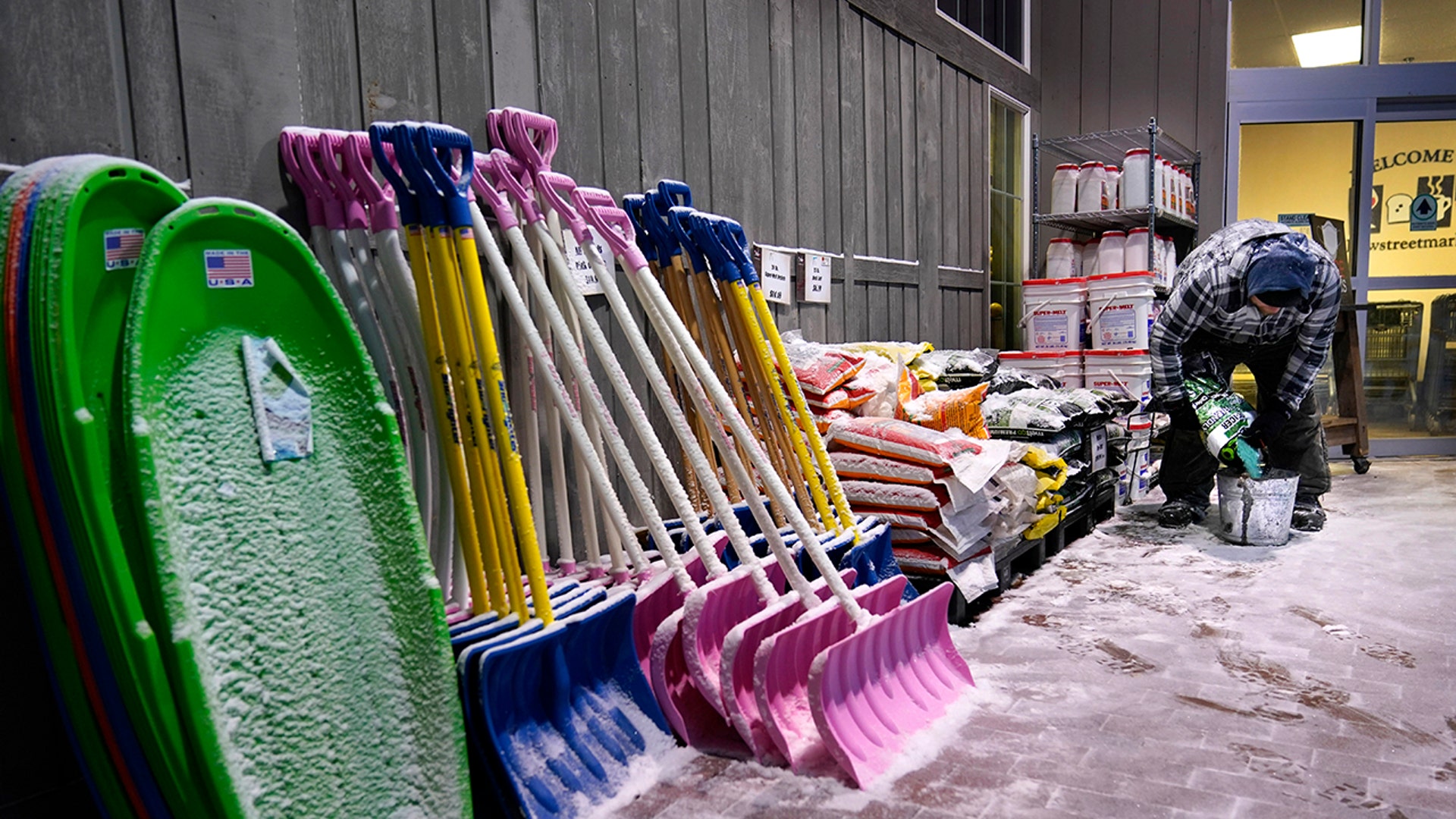 Rick Wallace fills a bucket with salt to melt snow on a sidewalk outside the Bow Street Market during a winter snow storm, Tuesday, Feb. 2, 2021, in Freeport, Maine. Sleds, shovels and salt will be popular items as the region is hit with its first major storm of the new year.