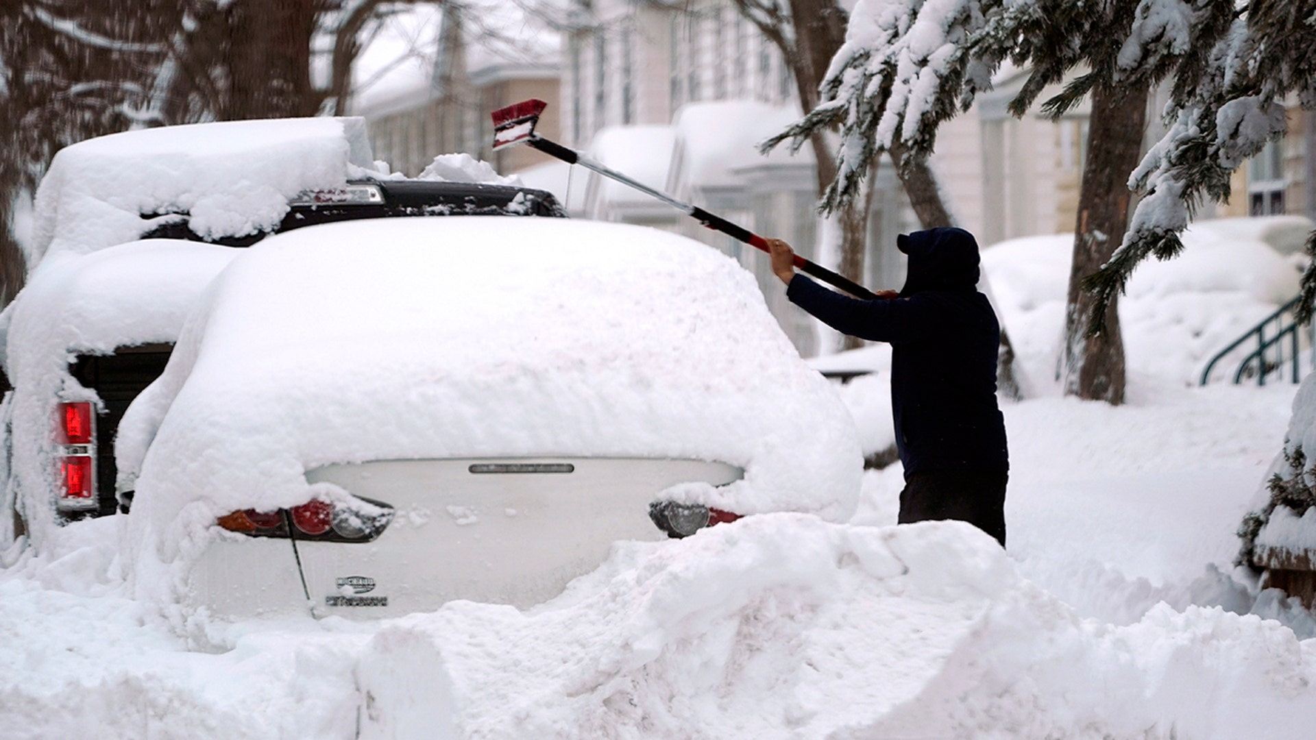 A man brushes snow off a car, Tuesday, Feb. 2, 2021, in Lawrence, Mass. A sprawling, lumbering winter storm has walloped the Eastern U.S., shutting down coronavirus vaccination sites, closing schools and halting transit.