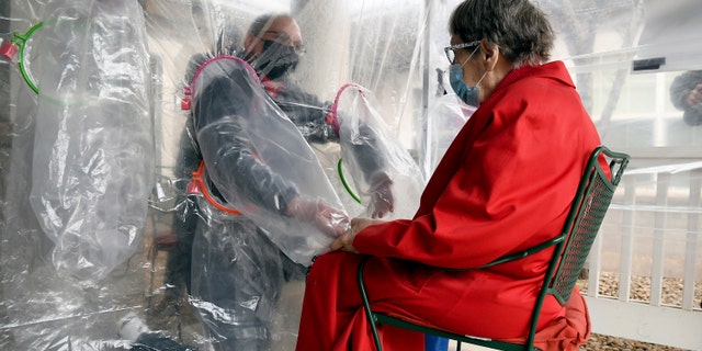 Gregg MacDonald holds hands with his 84-year-old mother, Chloe MacDonald, at the "hug tent" outside the Juniper Village assisted living center in Louisville, Colorado. (AP Photo/Thomas Peipert)