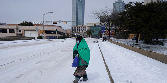 A woman wrapped in a blanket crosses the street near downtown Dallas on Tuesday, February 16, 2021. Temperatures dropped to single digits as snow cut air travel and grocery stores.  (Photo AP / LM Otero)