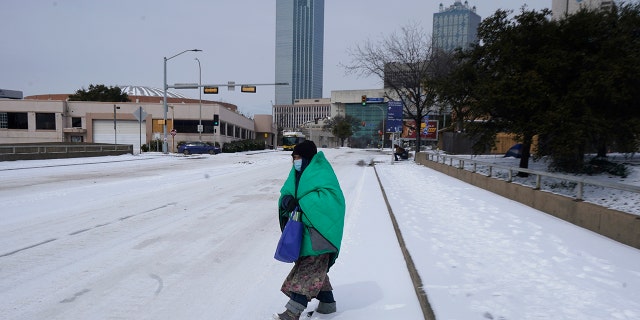 A woman wrapped in a blanket crosses the street near downtown Dallas on Tuesday, February 16, 2021. Temperatures dropped to single digits as snow cut air travel and grocery stores.  (Photo AP / LM Otero)