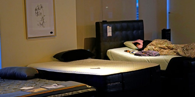 Dialina Gonzalez sleeps on a mattress inside a Gallery Furniture store which opened as a shelter Wednesday, Feb. 17, 2021, in Houston. Millions in Texas still had no power after a historic snowfall and single-digit temperatures created a surge of demand for electricity to warm up homes unaccustomed to such extreme lows, buckling the state's power grid and causing widespread blackouts. (AP Photo/David J. Phillip)