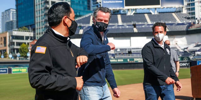 FILE: California Governor Gavin Newsom, center, bumps elbows with San Diego Mayor Todd Gloria after a news conference at Petco Park, which will host a vaccination site in a parking lot next to the ballpark in San Diego.