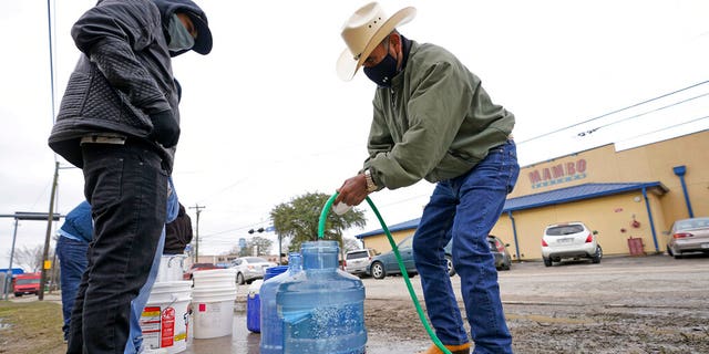 Leovardo Perez, right, fills a jug of water using a hose from a water tap at a public park Thursday, February 18, 2021, in Houston. 