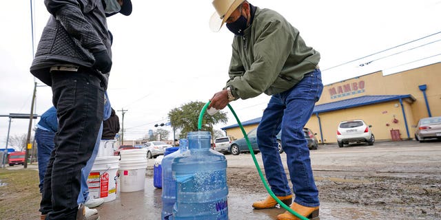 Leovardo Perez, right, fills a water jug using a hose from a public park water spigot Thursday, Feb. 18, 2021, in Houston. (Associated Press)