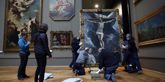 Workers handle a painting called 'Christ on the Cross Adored by Two Donors' by Spanish painter El Greco, in the Louvre museum, in Paris. (AP Photo/Thibault Camus)