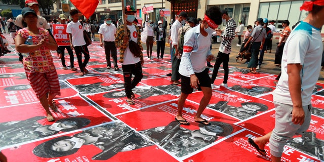 Anti-coup protesters step on posters with an image of a soldier and a Burmese sign that reads "armed terrorist" plastered on a road in Yangon, Burma Monday, Feb. 22, 2021. Protesters gathered in Burma's biggest city Monday despite the ruling junta's thinly veiled threat to use lethal force if people answered a call for a general strike opposing the military takeover three weeks ago. (AP Photos)