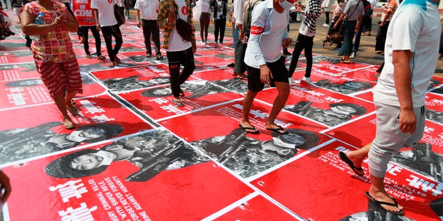 Anti-coup protesters step on posters with an image of a soldier and a Burmese sign that reads "armed terrorist" plastered on a road in Yangon, Burma Monday, Feb. 22, 2021. Protesters gathered in Burma's biggest city Monday despite the ruling junta's thinly veiled threat to use lethal force if people answered a call for a general strike opposing the military takeover three weeks ago. (AP Photos)