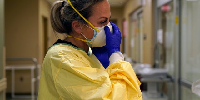 Registered nurse Chrissie Burkhiser puts on personal protective equipment as she prepares to treat a COVID-19 patient in the in the emergency room at Scotland County Hospital in Memphis, Mo. (AP Photo/Jeff Roberson, File)