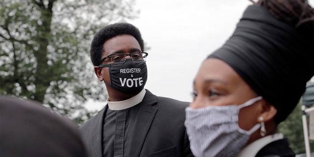 FILE - In this Monday, July 20, 2020 file photo, the Rev. Rahsaan Hall, of the St. Paul AME Church in Cambridge, Mass., wears a mask which reads, "Register &amp; Vote" outside the Statehouse in Boston. (AP Photo/Charles Krupa)